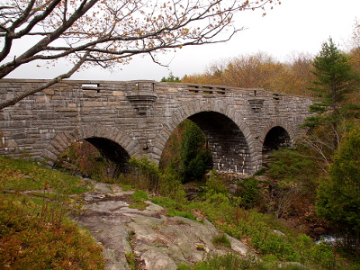 [Three arched stone bridge made with thin, rectangular, grey rock.]